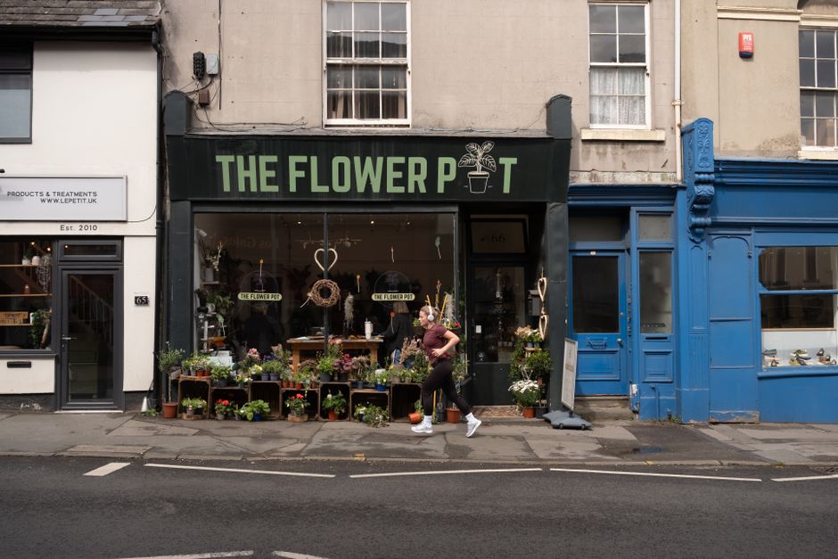 A storefront named 'The Flower Pot' displaying a variety of fresh floral arrangements in front of the shop. The flowers include vibrant pink, purple, white, and green blooms arranged in wooden crates