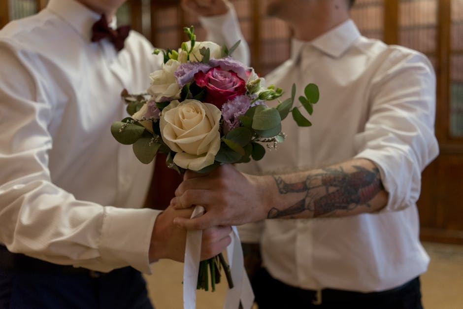 A floral arrangement featuring white and pale pink roses, purple lisianthus, and eucalyptus leaves, held by two individuals dressed in white shirts with the sleeves rolled up. One person has visible t