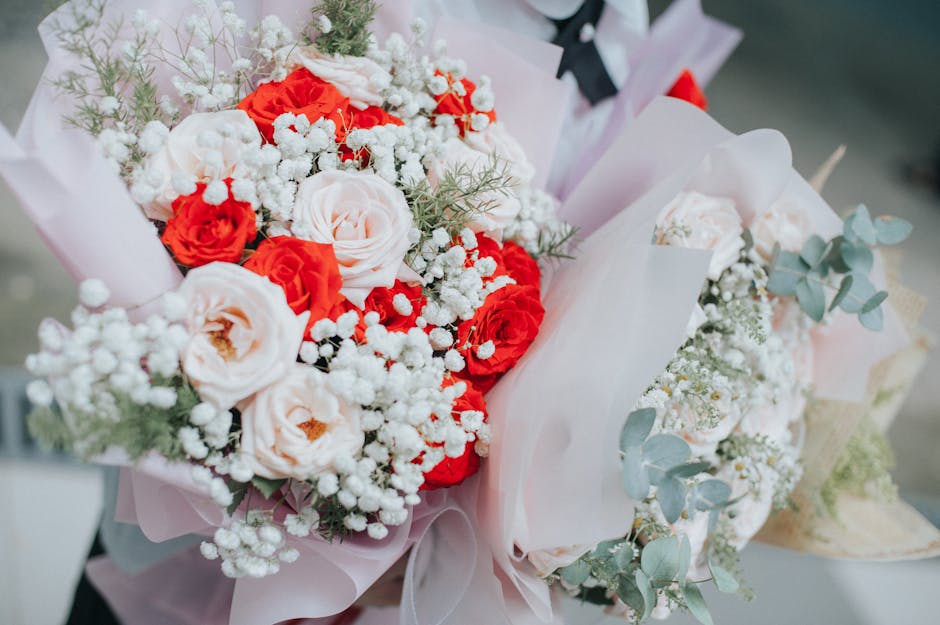 A vibrant floral bouquet featuring a mix of peach and bright red roses, complemented by delicate white baby's breath and soft green eucalyptus leaves. The flowers are arranged in a lush, rounded style