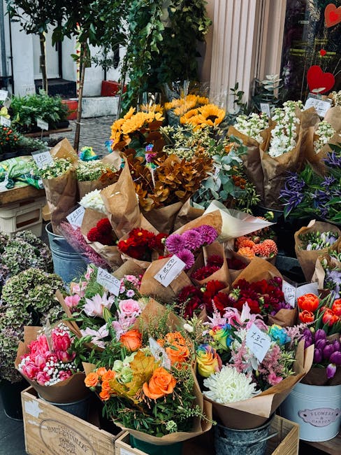 A vibrant display of freshly prepared flower bouquets arranged outdoors, featuring a variety of blooms such as sunflowers with bright yellow petals, pink lilies, orange roses, purple irises, white car